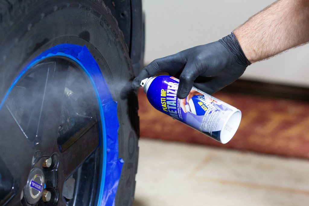 Hand spraying can of Plasti Dip on taped off car wheel rims
